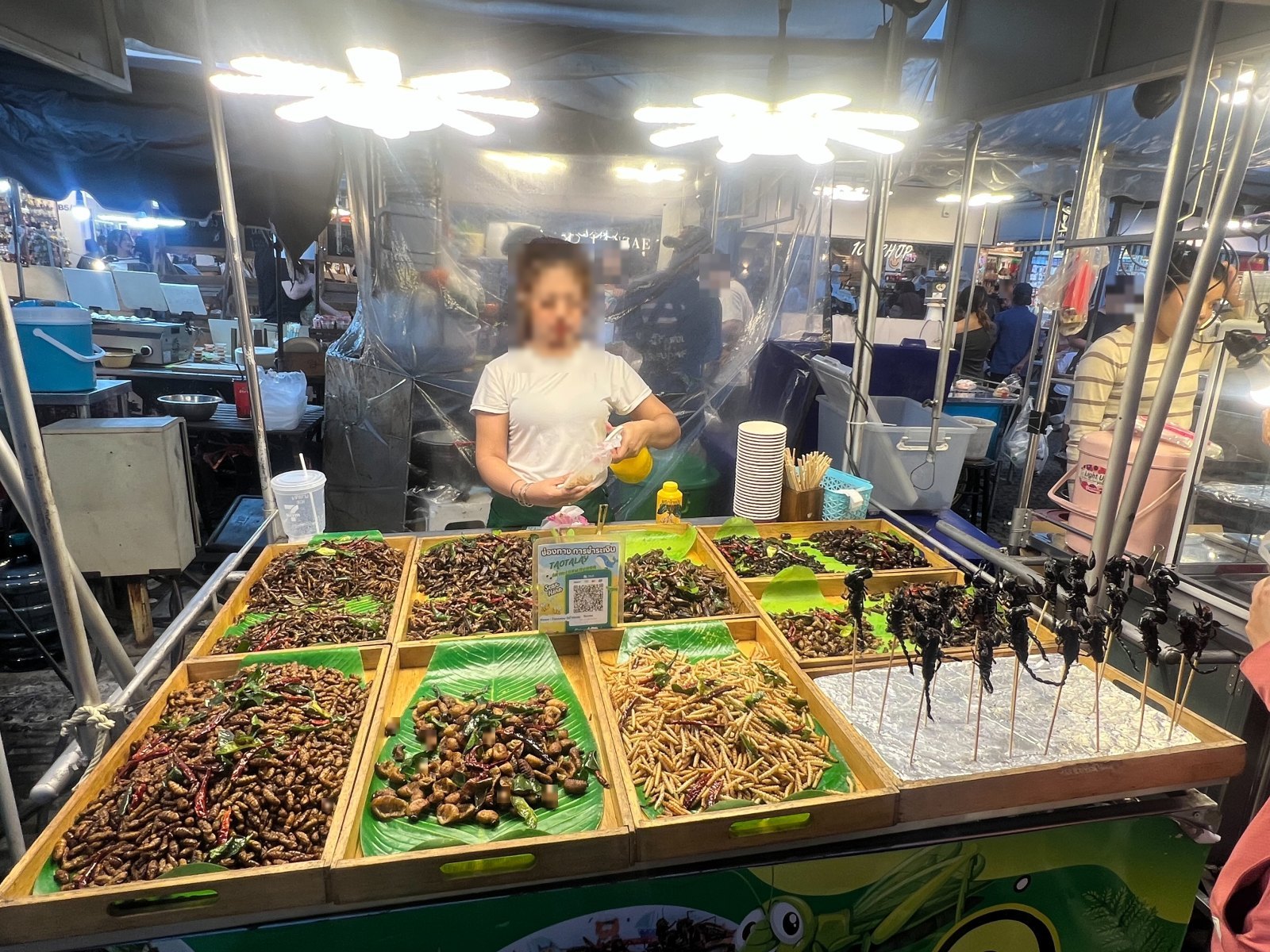 木の盆に山積みになった素揚げの昆虫と、緑のネオン看板