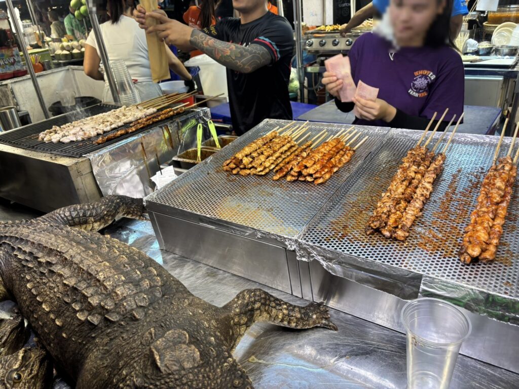台の上に一頭まるごと横たわるワニと、脇の串焼き