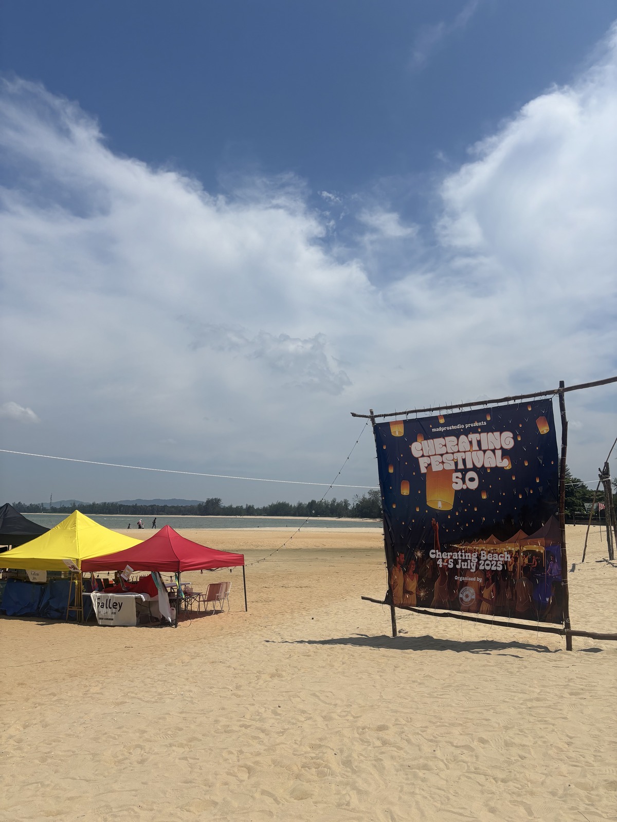 昼の砂浜に立つCherating Festival 5.0のバナーと黄色と赤のテント