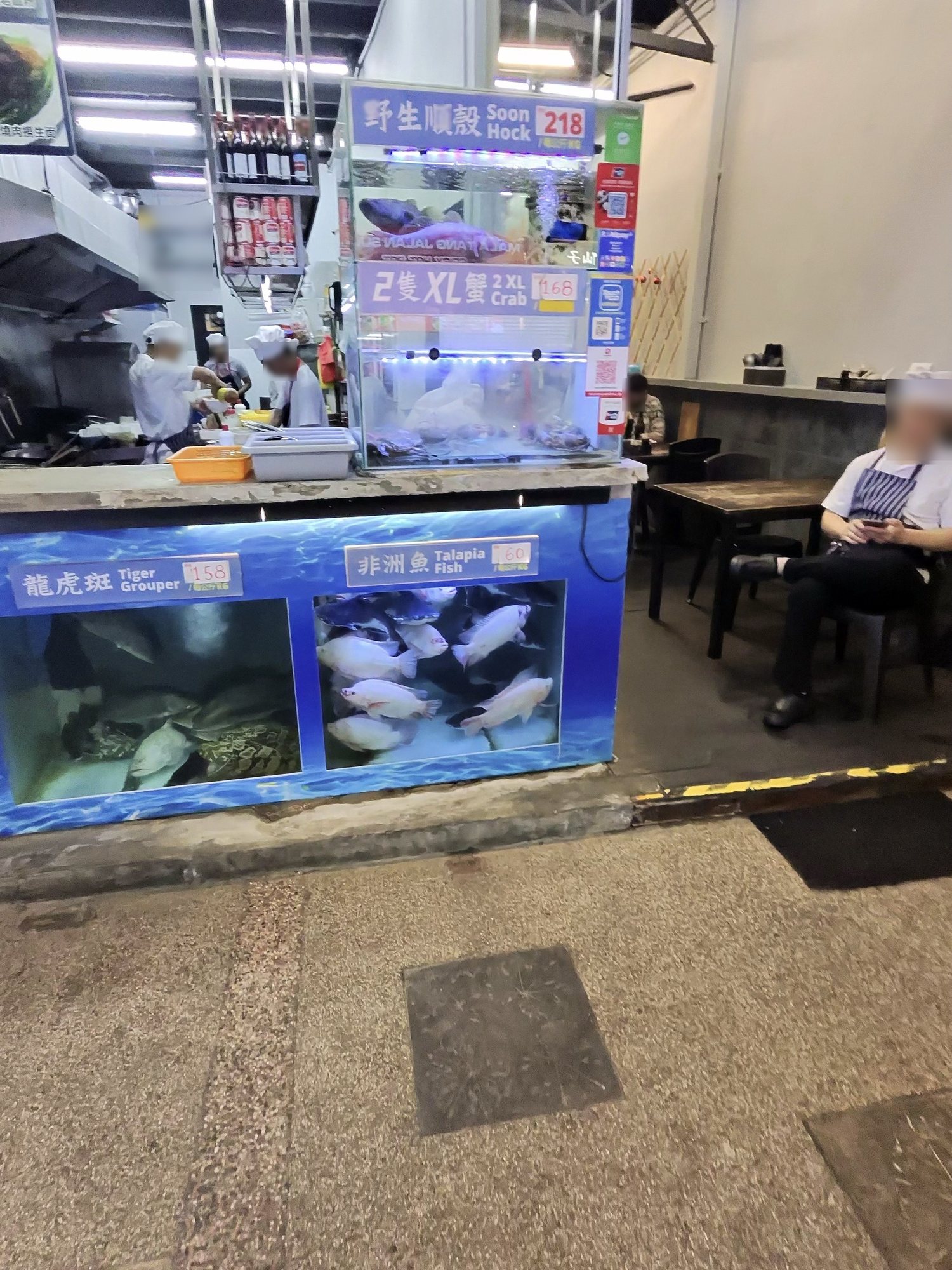 店先の水槽に魚、「Tiger Grouper」「Tilapia fish」の札。奥に厨房