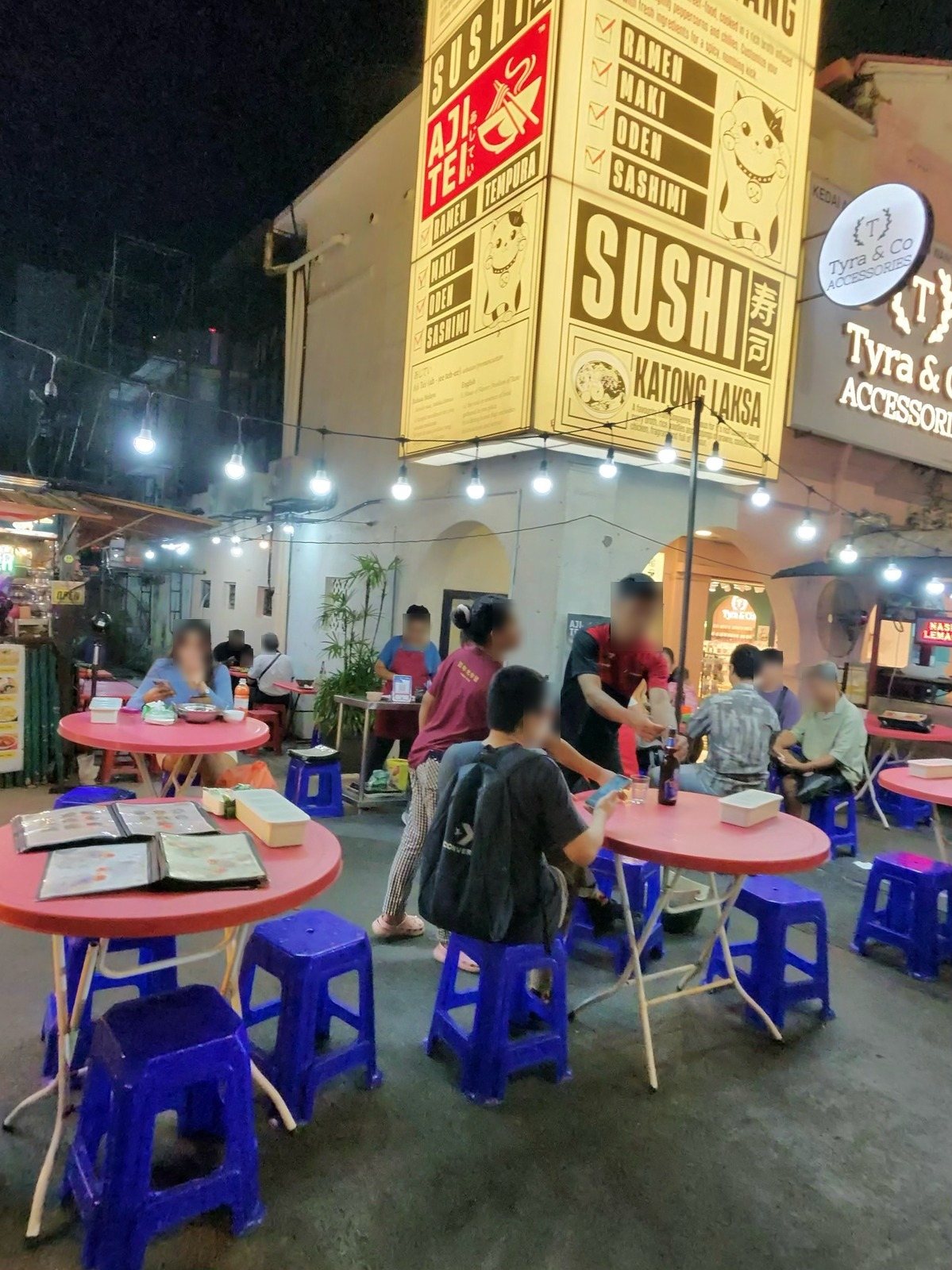 SUSHIの黄色い看板の下のピンクのテーブルと青い椅子